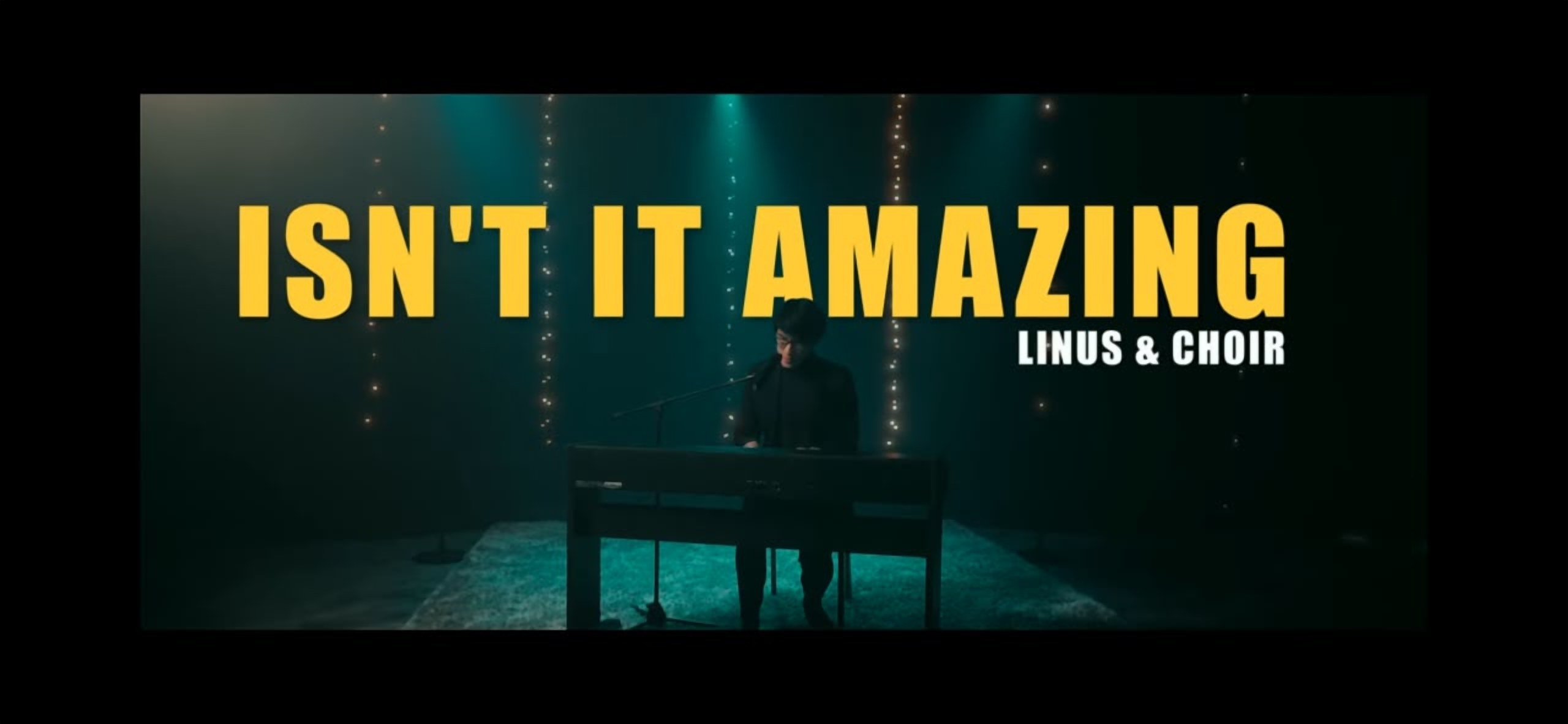 A still from the LoudVoice music video “Isn't It Amazing” — Linus at the piano with the choir title card