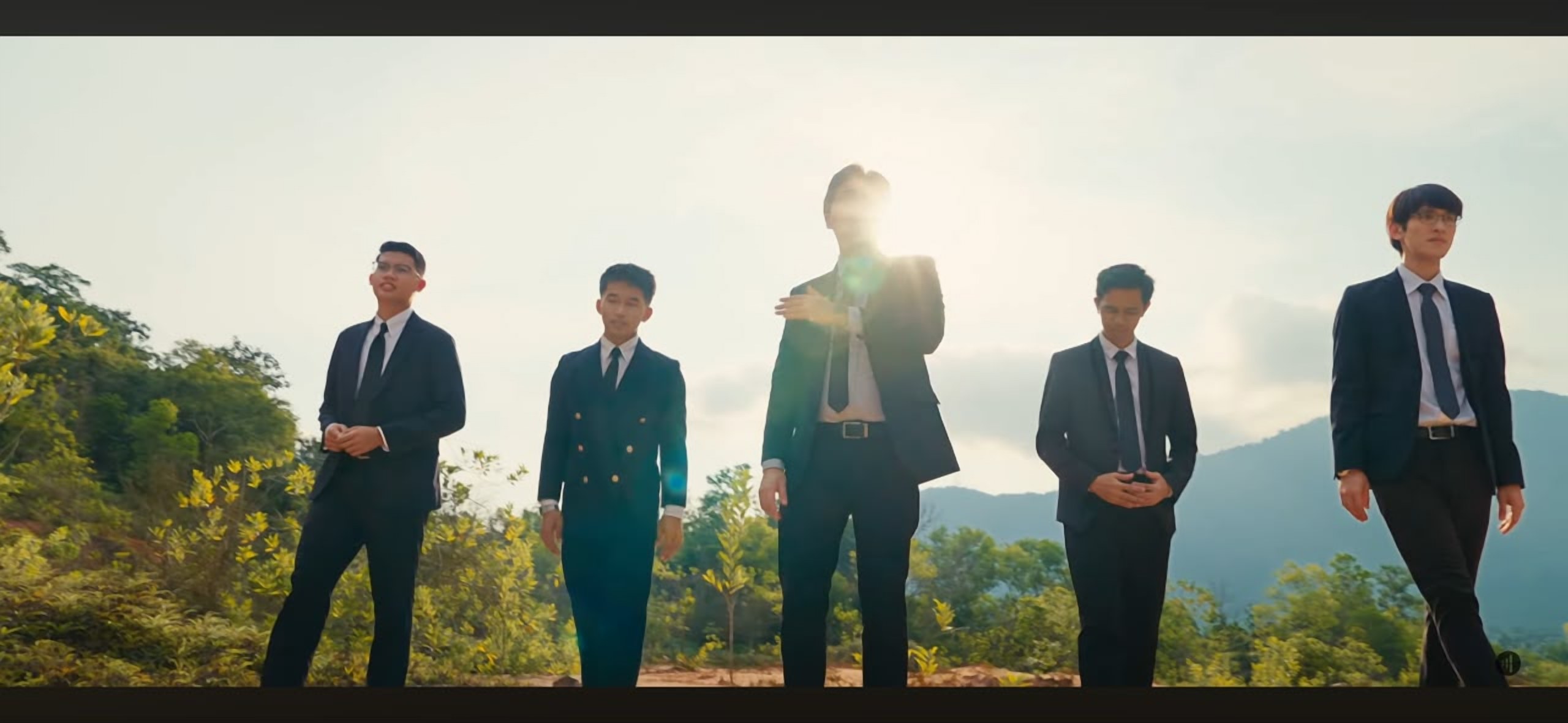 A still from a LoudVoice music video — five singers in suits standing outdoors against the sun