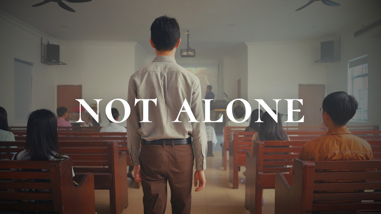 Thumbnail for the music video &ldquo;My High Priest | He Intercedes for Me&rdquo; — a young man standing in a church aisle beneath the words &lsquo;Not Alone&rsquo;