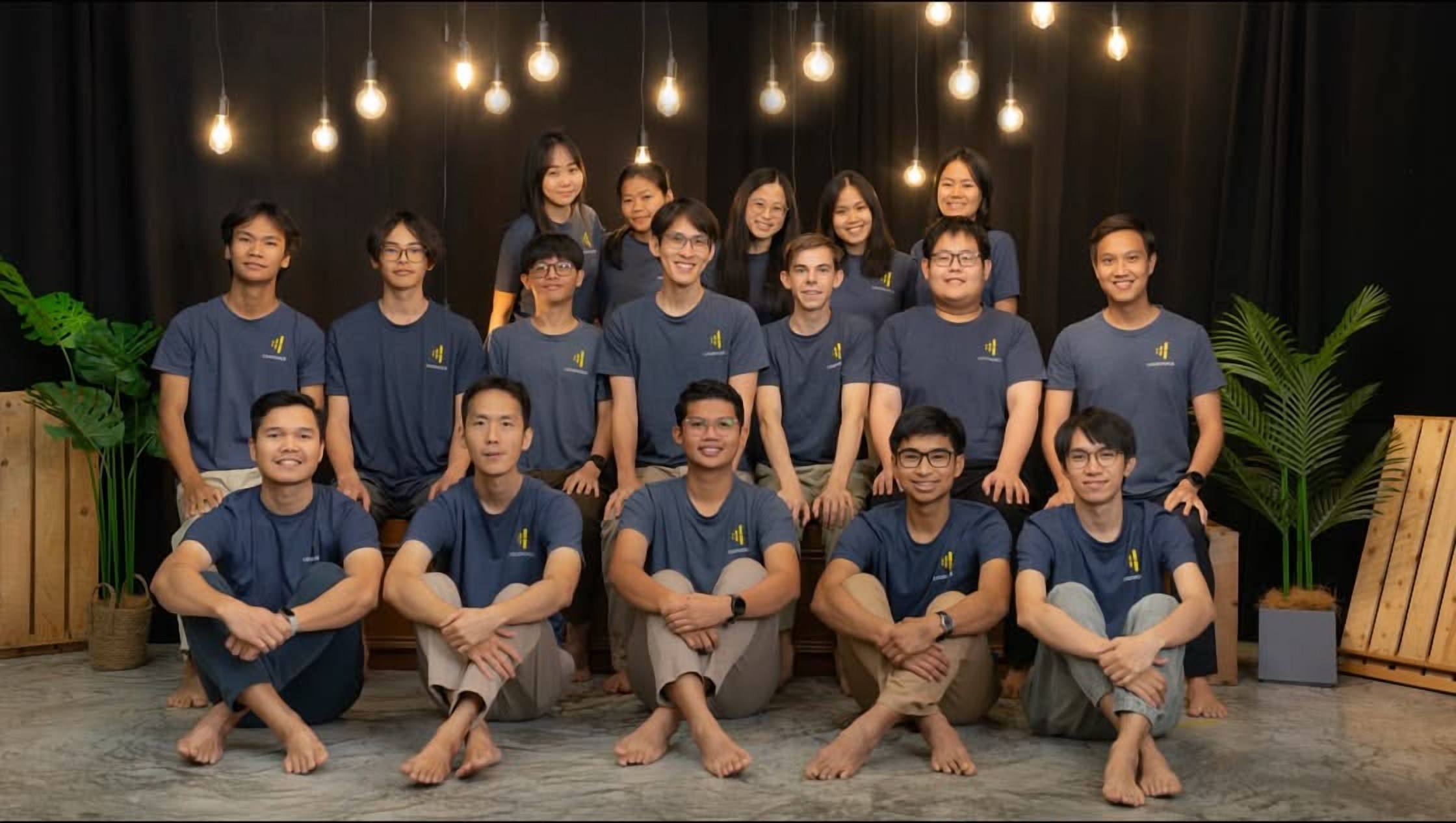 The LoudVoice volunteer team in navy LoudVoice shirts, group portrait in the studio beneath hanging Edison bulbs