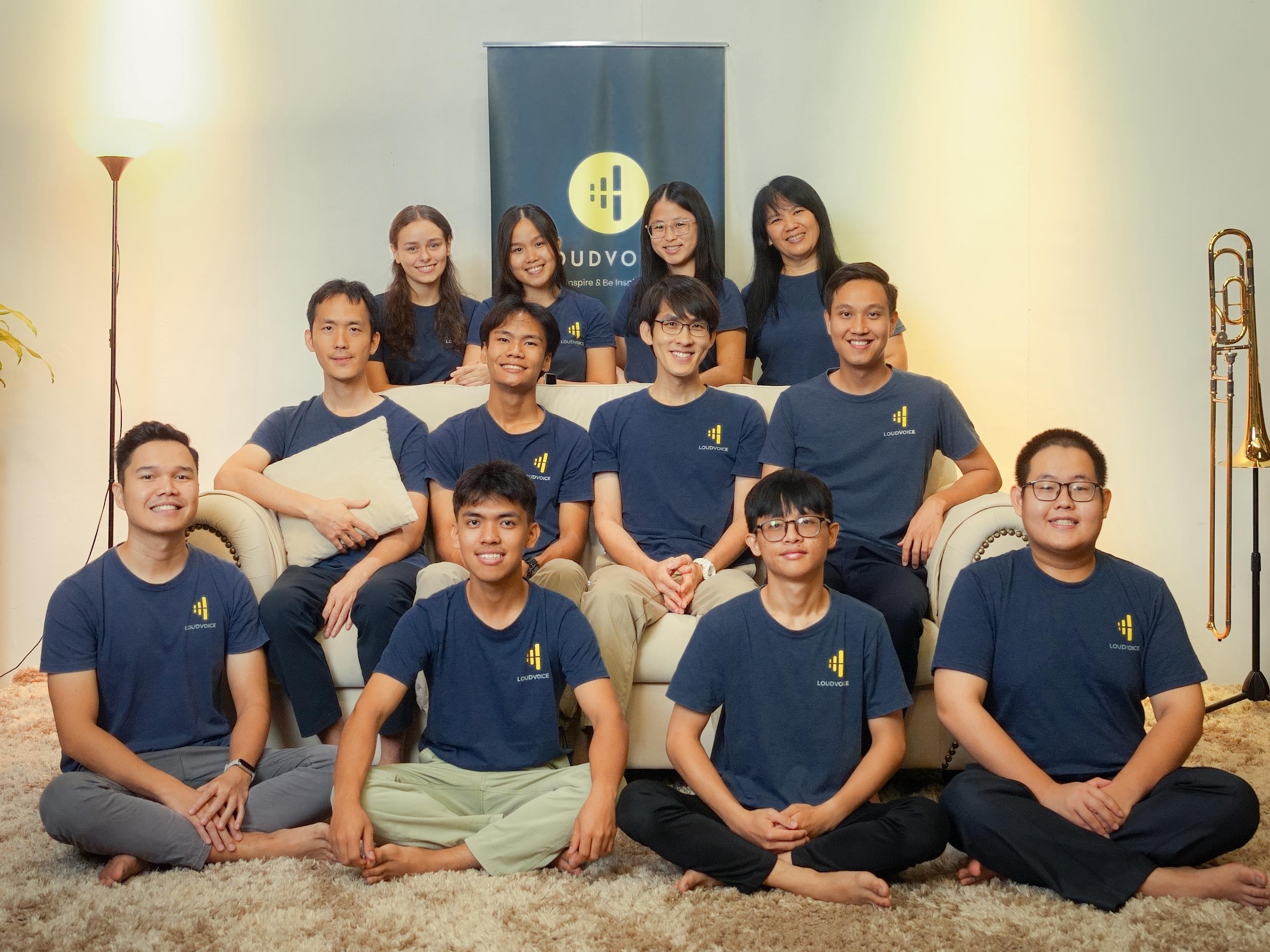 Twelve volunteers and team in navy LoudVoice shirts posed on and around the couch in front of a LoudVoice banner, smiling at the camera